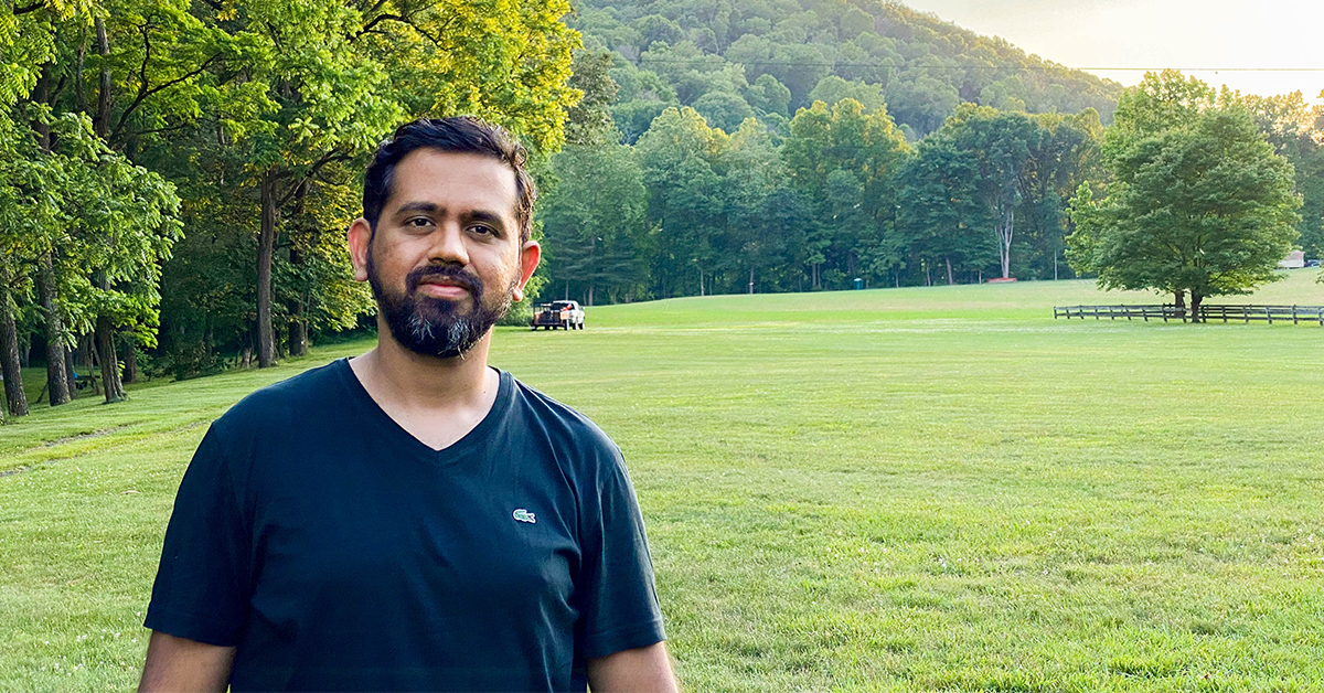 Swapnil Shinde, Capital One data and machine learning engineer, stands on a field of grass in front of trees